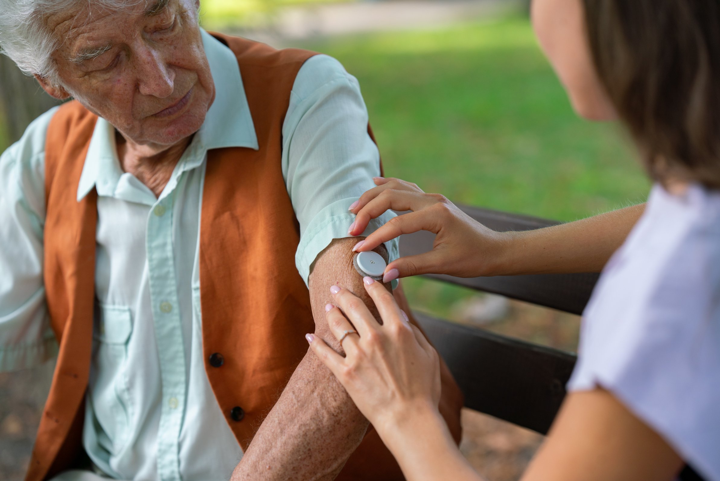 Caregiver Helping Senior Diabetic Man to Apply Continuous Glucose Monitor Sensor on His Arm.